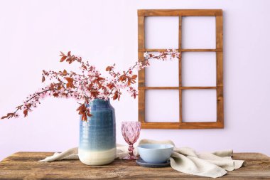 Çiçek açan ağaç dalları, cam, kase ve peçeteyle pembe duvarın yanındaki ahşap masada.