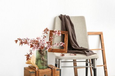 Ağaç dalları olan vazo ahşap çekmecede ve beyaz duvarın yanında sandalye.