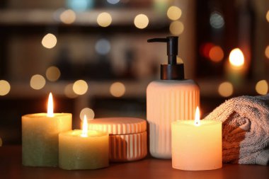 Yanan mumlar, banyo malzemeleri ve bulanık ışıklara karşı masaya sarılmış havlu.