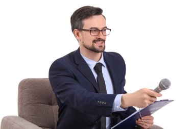 Beyaz arka plandaki koltukta mikrofonu ve panosu olan erkek gazeteci