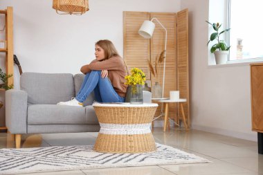 Evdeki kanepede oturan düşünceli genç bayan.