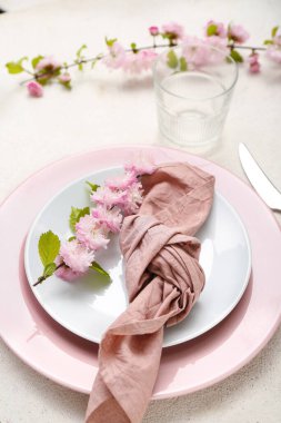 Çatal bıçak takımı, çiçek açan ağaç dalları ve beyaz grunge arka planda katlanmış peçeteyle servis edilen güzel bir masa.