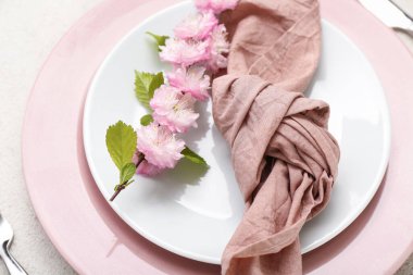 Çatal bıçakla servis edilen güzel masa, çiçek açan ağaç dalı ve beyaz grunge arka planda katlanmış peçete.