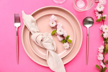 Çatal bıçak takımı, çiçek açan ağaç dalları ve pembe arka planda katlanmış peçeteyle servis edilen güzel bir masa.