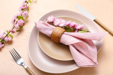 Çatal bıçak takımı, çiçek açan ağaç dalları ve bej arka planda katlanmış peçeteyle servis edilen güzel bir masa.