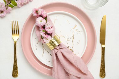 Çatal bıçak takımı, çiçek açan ağaç dalları ve beyaz arka planda katlanmış peçeteyle servis edilen güzel bir masa.
