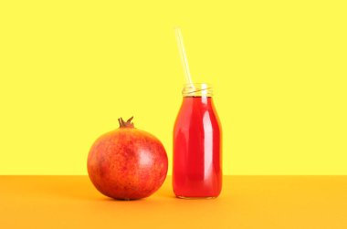 Sarı zemin üzerinde bir şişe taze nar suyu.