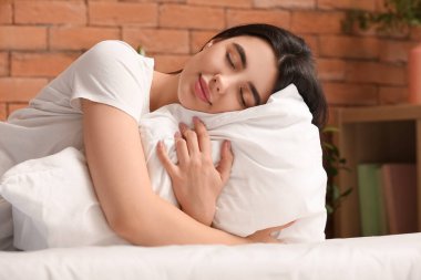 Genç bir kadın yatak odasında yumuşak yastığa sarılıyor.