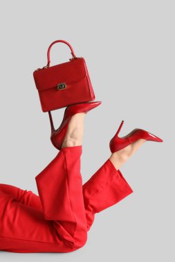 Kırmızı topuklu kadın bacakları, gri arka planda çanta.