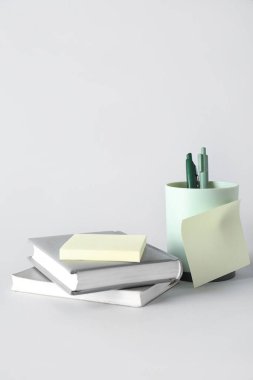 Gri arkaplan üzerine yapışkan notları ve kitapları olan kalem tutucu