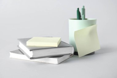 Gri arkaplan üzerine yapışkan notları ve kitapları olan kalem tutucu