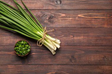 Bir demet taze soğan ve ahşap arka planda kesilmiş kase.