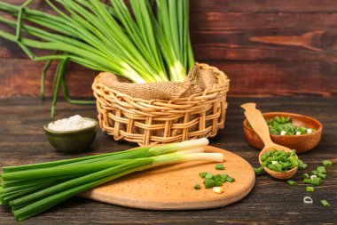 Board with fresh green onion on wooden background