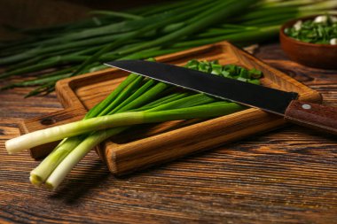 Board with fresh green onion on wooden background