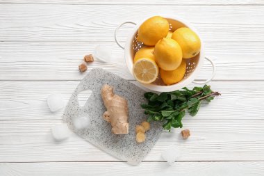 Beyaz ahşap zemin üzerinde limon, nane, buz küpleri ve zencefil olan bir tahta.