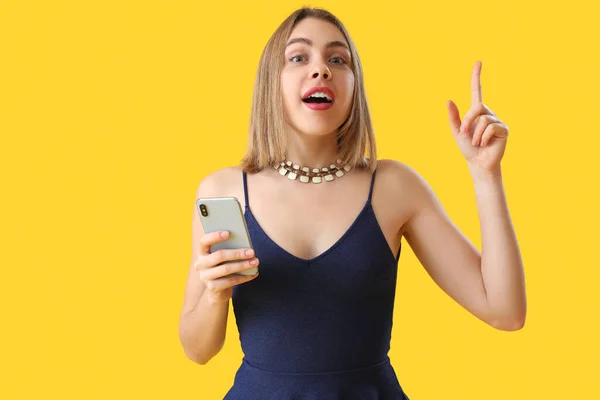 黄色の背景に何かを指している携帯電話を持つ若い女性 — ストック写真