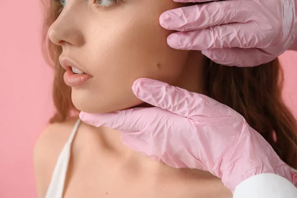 皮肤科医生根据粉红背景和特写镜头检查年轻女子脸上的痣 — 图库照片