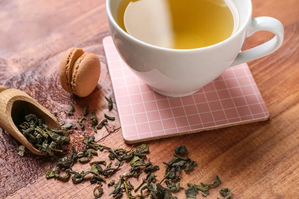 Drink coaster with cup of tea, macaroon and scattered leaves on wooden table, closeup