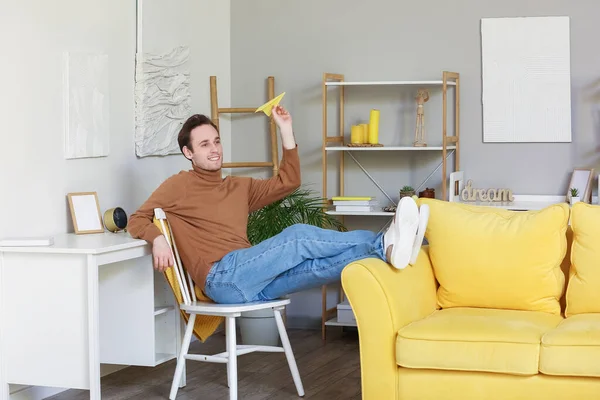 Young man throwing paper plane at home