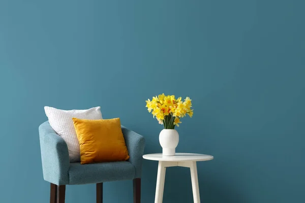 青い壁の近くのコーヒーテーブルの上にクッションと開花ナルシスの花を持つ居心地の良いアームチェア — ストック写真
