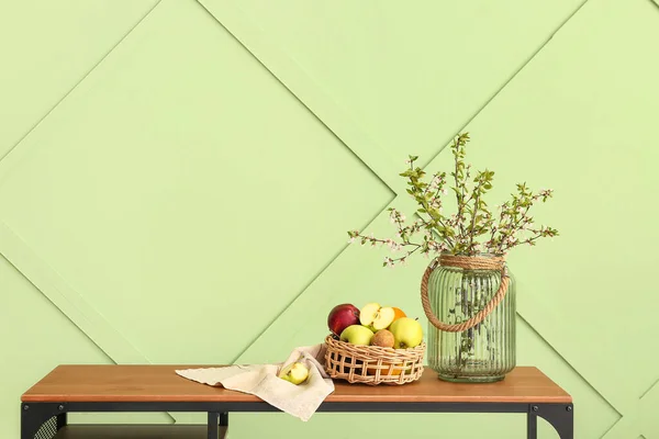 緑の壁の近くの木製のテーブルの上に木の枝やフルーツバスケットが咲く花瓶 — ストック写真