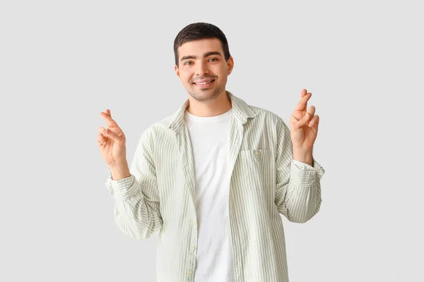 Young man crossing fingers on light background