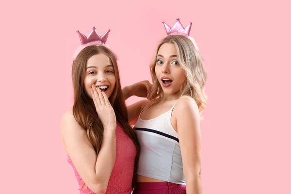 Surprised young sisters in crowns on pink background