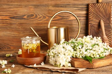 Sulama tenekesi, bal kavanozu ve ahşap masa üzerinde beyaz leylak dalları olan kompozisyon