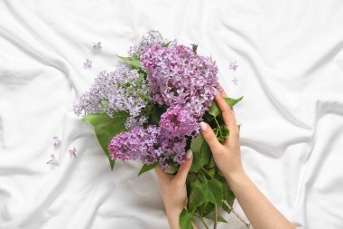 Yatağında çiçek açan leylak çiçekleri olan kadın elleri.