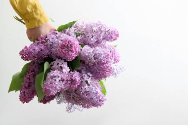 Beyaz duvarın yanında güzel leylak çiçeklerinden bir buket tutan kadın.