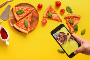 Sarı arka planda lezzetli pizza margaritasının fotoğrafını çeken bir kadın.