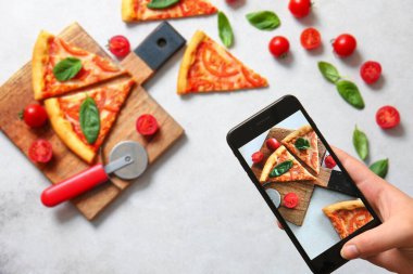 Beyaz grunge arka planda lezzetli pizza margaritasının fotoğrafını çeken bir kadın.