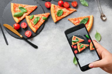 Kadın grunge grisi arka planda lezzetli pizza margaritasının fotoğrafını çekiyor.