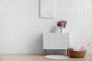 İçinde leylak çiçekleri olan vazo ve odadaki çekmecelerin üzerindeki ayna.