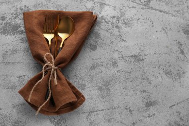 Altın çatal, bıçak ve kaşık, gri arka planda peçete.