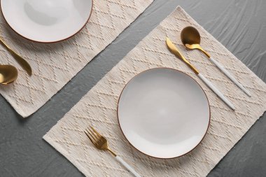 Altın çatal bıçak seti, gri masada tabak ve mutfak paspası.