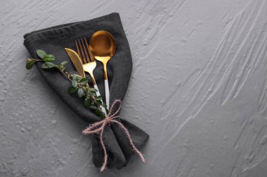 Altın çatal bıçak seti, gri arka planda siyah peçeteye konmuş.