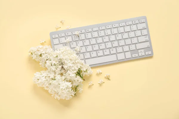 Beautiful lilac flowers with PC keyboard on pale yellow background