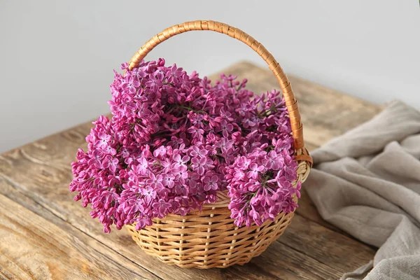 Wicker basket of beautiful lilac flowers on wooden table