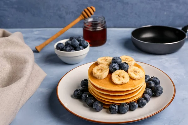 Plate with tasty pancakes, banana and blueberry on blue background, closeup