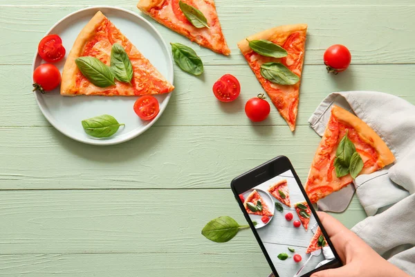 Yeşil ahşap arka planda lezzetli pizza margaritasının fotoğrafını çeken bir kadın.