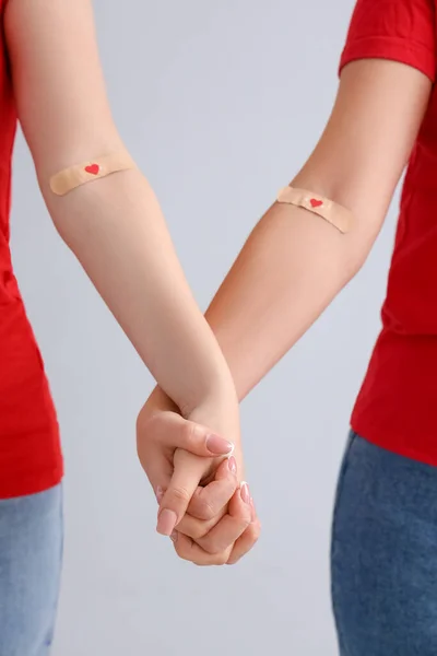 Female Blood Donors Applied Medical Patches Holding Hands Light Background — Stock Photo, Image