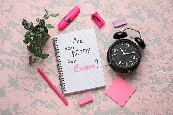 Notebook with question ARE YOU READY FOR EXAM?, alarm clock and different stationery on grunge pink background