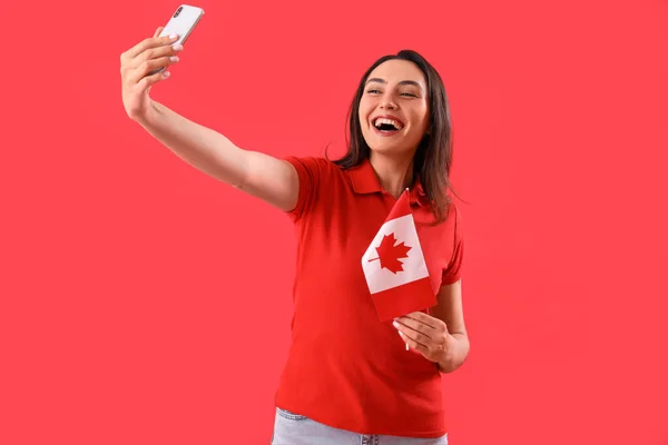 拿着加拿大国旗的年轻女子带着红色背景的自拍 — 图库照片