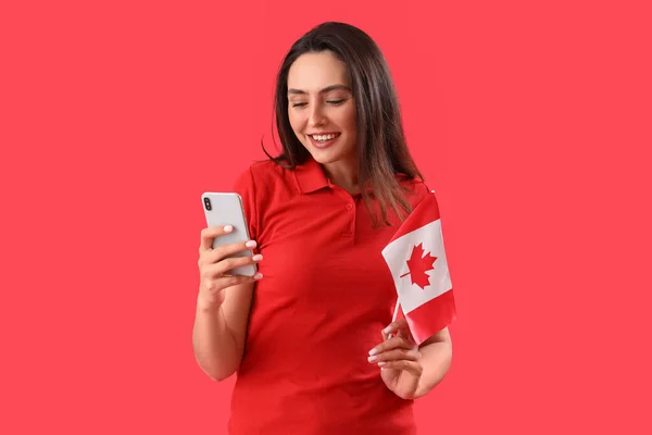 拿着加拿大国旗的年轻妇女使用红色背景的手机 — 图库照片