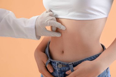 Dermatolog bej arka planda genç kadının benini inceliyor.