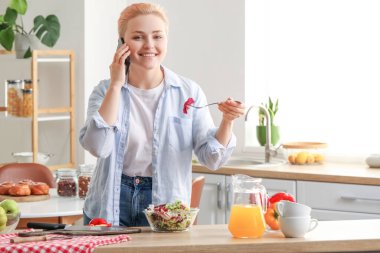 Sebze salatalı genç bir kadın mutfakta cep telefonuyla konuşuyor.