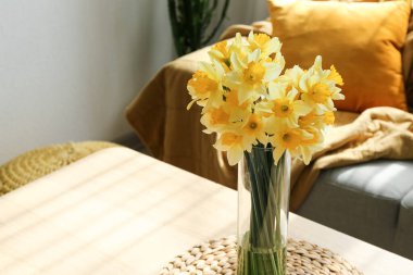 Aydınlık oturma odasındaki masada çiçekli vazo, yakın plan.