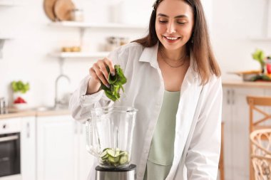 Genç bir kadın mutfakta ıspanağı blender 'a koyuyor.