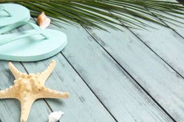 Parmak arası terlik, deniz yıldızı, deniz kabuğu ve ahşap arka planda palmiye yaprağı kompozisyonu